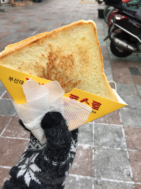 #釜山大學名物吐司명물토스트
在釜山大學商圈中,因多數消費者都是大學生,所以這裡的美食可是走平價路線~而位在釜山大學校園外的名物吐司,在釜山大學生的心中也是不可或缺的早餐美食啊~
土司烤的恰當好處,裡面的餡料更是一點也不馬虎,三層裡可都是塞得滿滿啊!有火腿、起司、蛋、苜蓿芽,酸黃瓜,加上特製的醬料,吃一次後你就會忘不了的好味道!如果不知道該怎麼點餐了話,只要跟店家講「special」就好。
